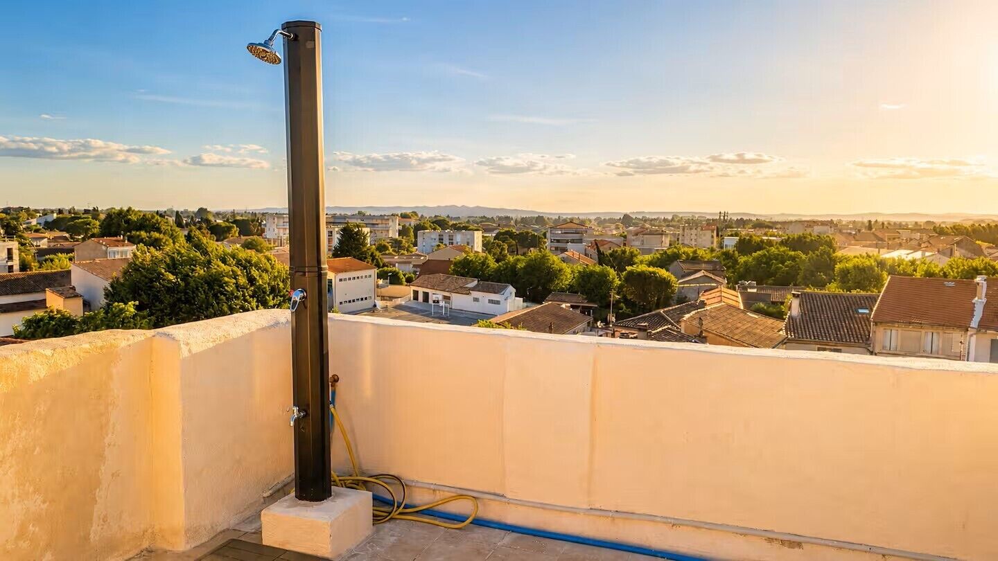 A rooftop with a water pipe, a metal pole, and a view of a residential area with houses and trees.