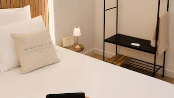 Quarto de hotel com uma cama, uma mesa de cabeceira com abajur, um guarda-roupa de metal preto e uma toalha sobre a cama.