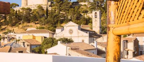 Vista de un pueblo histórico con un castillo destacado, una iglesia con campanario y una pared blanca con el texto 'Rooftop Sunset'.
