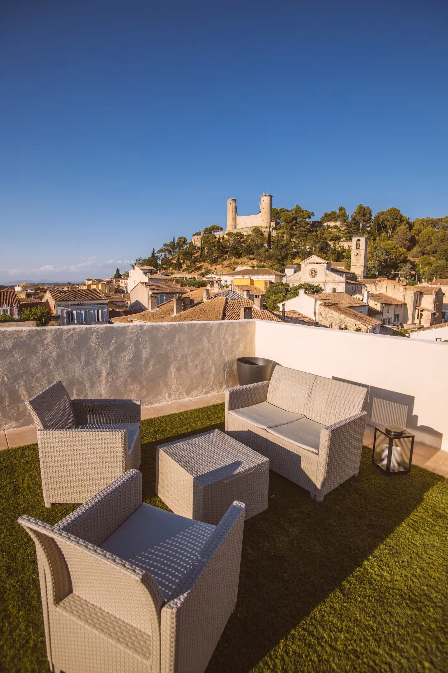Terraço no telhado com mobiliário de vime, vista clara de um castelo histórico e uma cidade abaixo.