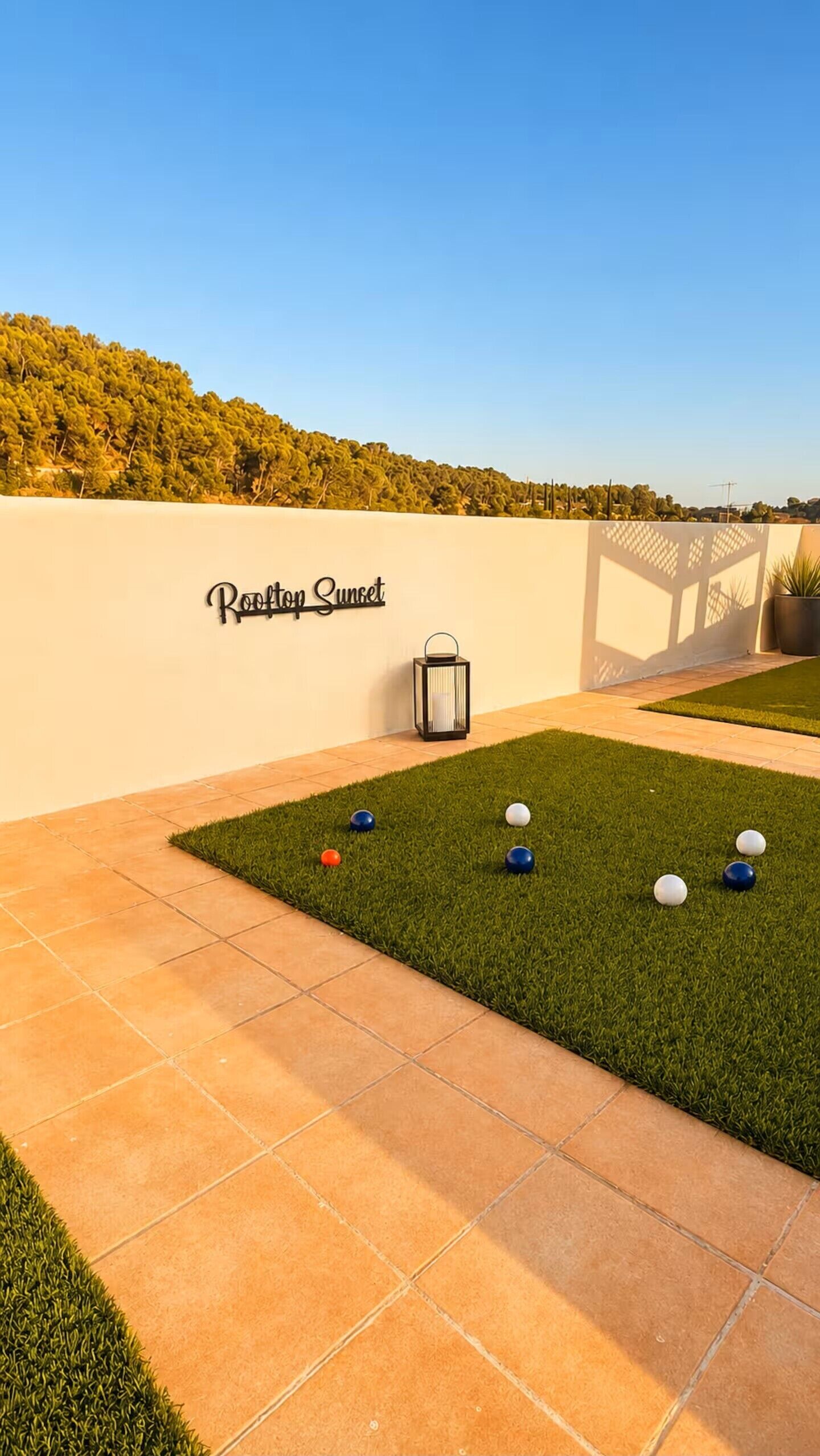 Une terrasse sur le toit avec une enseigne indiquant « Vue sur le coucher de soleil », une petite pelouse avec des balles de croquet et une lanterne.