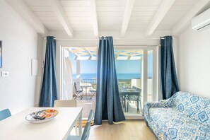 Ett rum med ett vitt tak, en mönstrad soffa, ett matbord med en tallrik på och en utsikt genom en glasdörr.