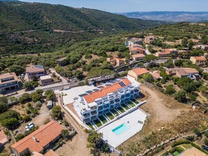 An aerial view of a residential area with a modern building featuring a swimming pool, surrounded by houses and greenery. - Affittimoderni Trinità D'Agultu - Vacation Rental (Trinità d´Agultu e Vignola)