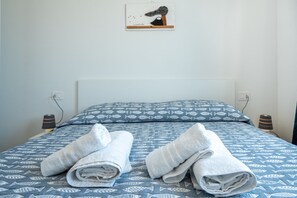 A neatly made bed with a patterned blue and white bedding, two rolled towels on the bed, and a small artwork on the wall. - Affittimoderni Trinità D'Agultu - Vacation Rental (Trinità d´Agultu e Vignola)