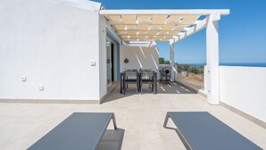 Eine Dachterrasse mit einer Pergola, einem Tisch mit Stühlen und Meerblick.