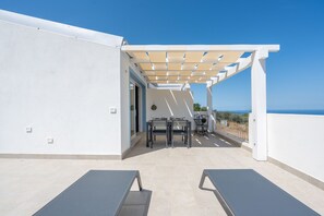 Eine Dachterrasse mit einer Pergola, einem Tisch mit Stühlen und Meerblick.