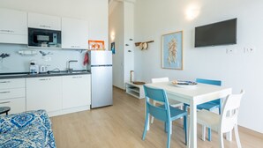 Eine moderne Küche mit weißen Schränken, einer Bosch-Mikrowelle und einem Kühlschrank. Es gibt eine Essecke mit einem wei ßen Tisch und blauen Stühlen.