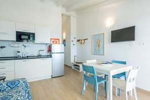 A modern kitchen with white cabinets, a Bosch microwave, and a refrigerator. There is a dining area with a white table and blue chairs.