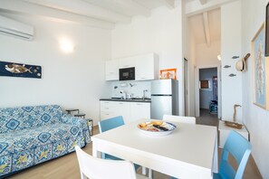 A compact living space with a kitchenette, a dining table with chairs, a sofa, and a kitchen counter.