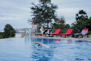 A swimming pool with a person swimming, red lounge chairs, and trees in the background. - Thaulle Luxury Boutique & Social Club  (Kirinda)