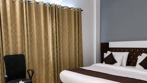A hotel room with a bed, a desk, a chair, a ceiling fan, and an air conditioning unit. - HOTEL K11 (Haldwani)