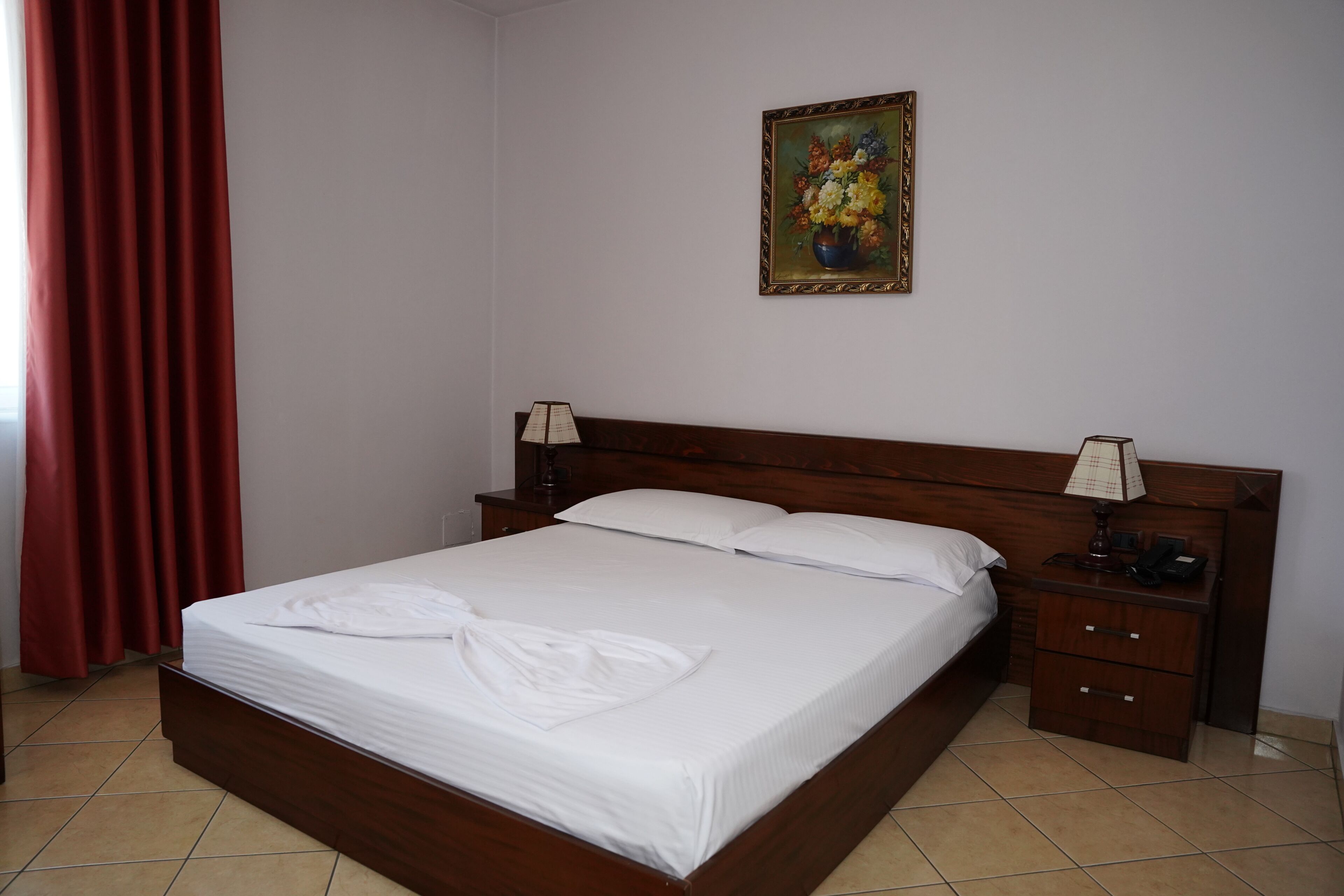 Un lit bien fait, avec du linge de lit blanc, dans une chambre dotée d’une tête de lit en bois, d’une table de chevet avec une lampe et d’un tableau au mur.