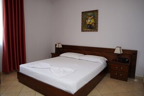 A neatly made bed with white linens in a room with a wooden headboard, a nightstand with a lamp, and a painting on the wall.