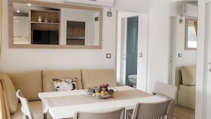 Un salon moderne avec un canapé blanc, une table à manger avec des chaises, un miroir et un appareil de climatisation.