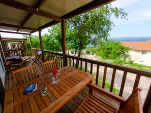Eine Holzterrasse mit Tisch und Stühlen, die einen schönen Ausblick auf eine Landschaft mit Bäumen und Meer bietet.