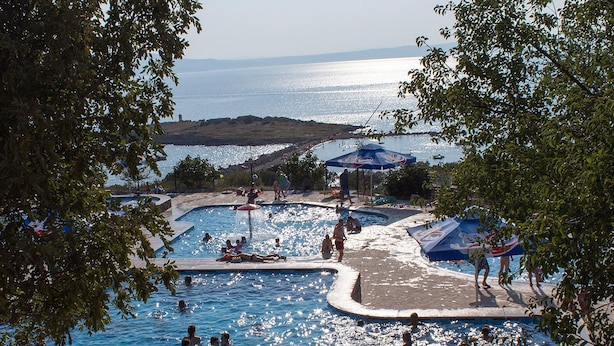 Un espace piscine comprenant plusieurs bassins, entouré d’arbres et offrant une vue sur la mer.