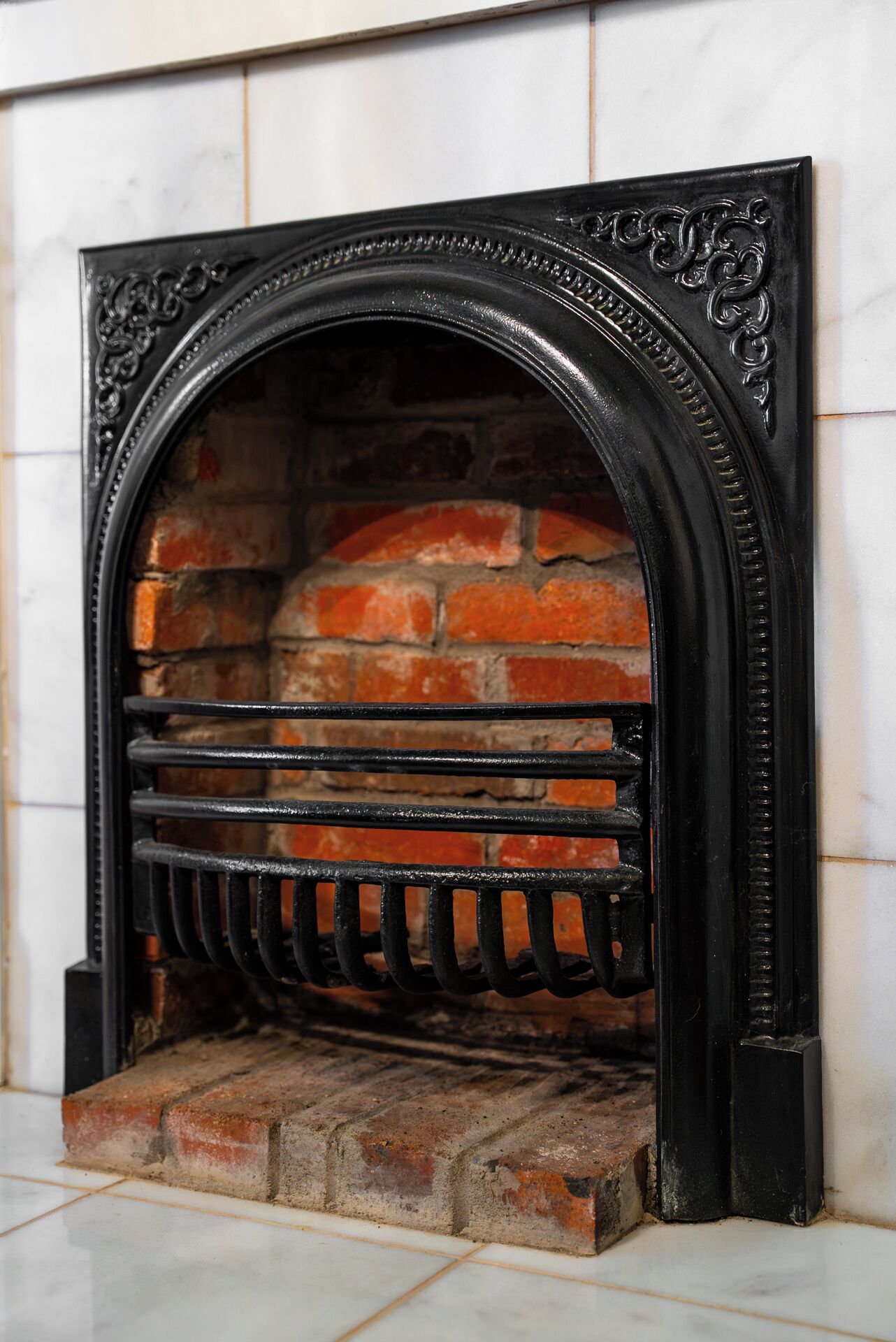 Una chimenea con interior de ladrillo, una rejilla metálica y un marco negro decorativo.