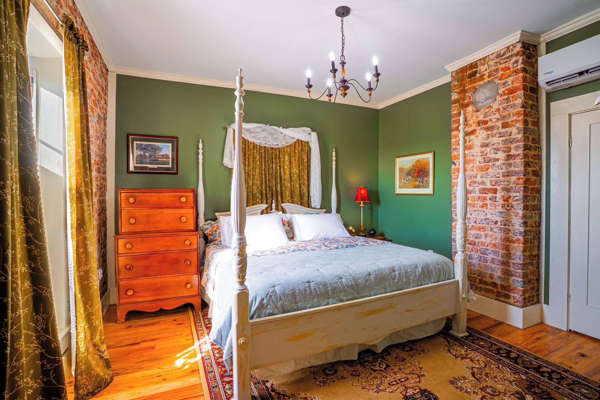 Un lit à baldaquin, une commode, une lampe rouge et un mur en briques.