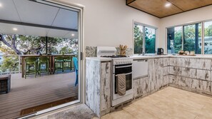A kitchen with a large island, a dining area with chairs, and a view of trees. - GULL COTTAGE - SUNRISE AT 1770 (AGNES WATER)