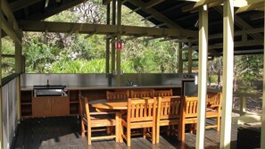 An outdoor kitchen area with a sink, a grill, and wooden furniture. - GULL COTTAGE - SUNRISE AT 1770 (AGNES WATER)