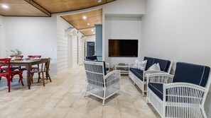 A modern living room with a dining area, white wicker furniture, a flat-screen TV, and a wooden ceiling. - GULL COTTAGE - SUNRISE AT 1770 (AGNES WATER)