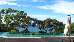 Ein Pool ohne Ende mit einer Holzterrasse, Blick auf den Strand und einem Strandsonnenschirm.