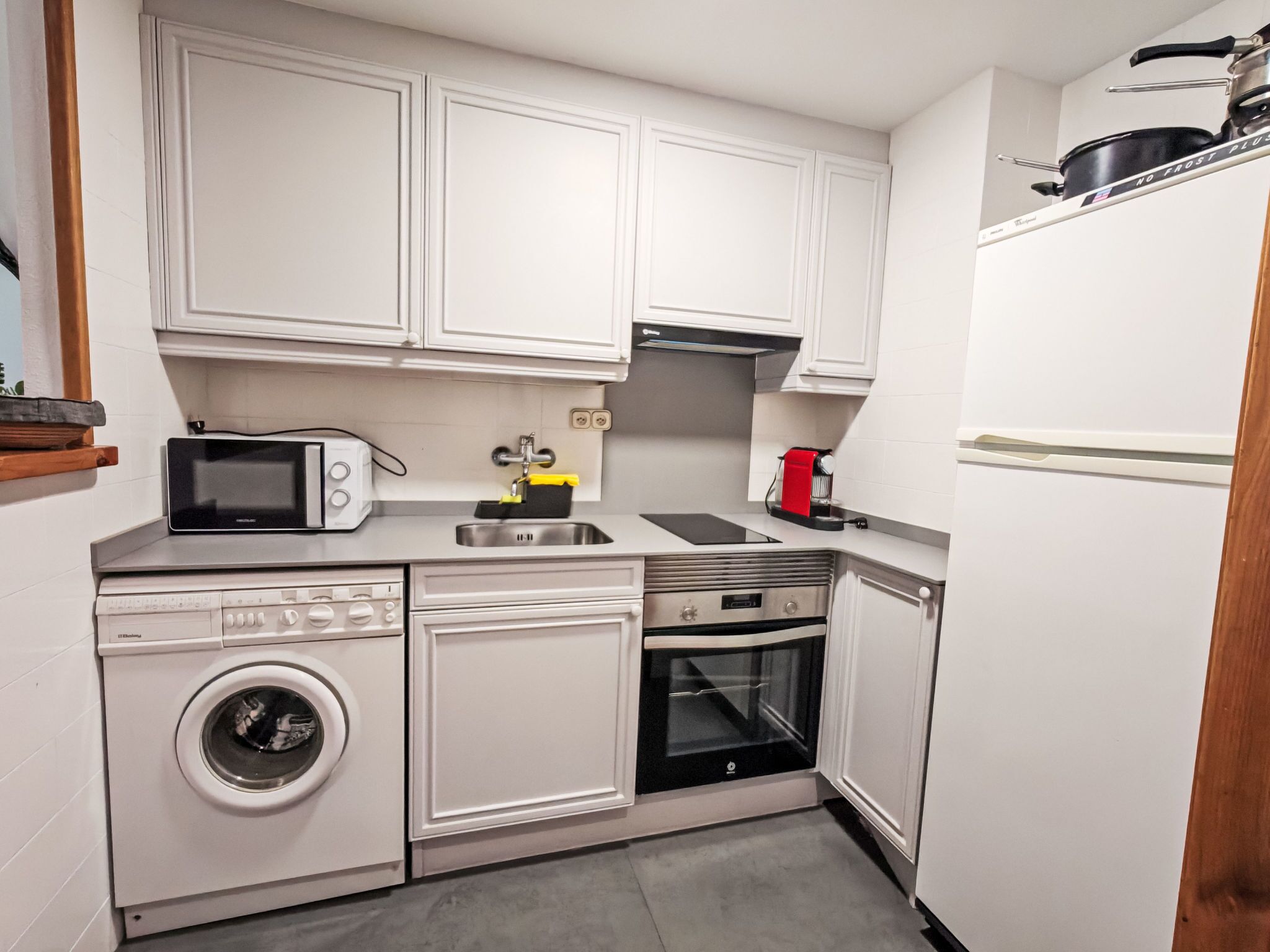 A compact kitchen with a microwave, toaster, sink, stove, oven, and a washing machine.