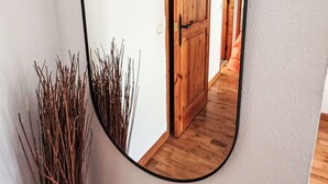 Un espejo refleja un pasillo con puertas de madera y una planta al lado.