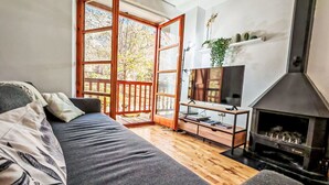 Una habitación acogedora con sofá, televisión, chimenea y un ventanal con vistas a árboles.