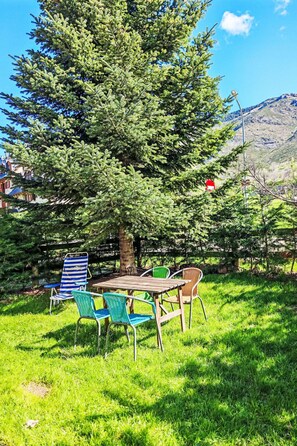 Ein Picknicktisch mit Stühlen, ein großer Baum und ein Berg im Hintergrund.