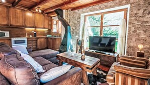 A cozy living area with a sofa, TV, and wooden furniture against a stone wall. - Apartamento - Puig Falcó 3 by Interhome (Taüll)