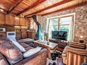 A cozy living area with a sofa, TV, and wooden furniture against a stone wall. - Apartamento - Puig Falcó 3 by Interhome (Taüll)