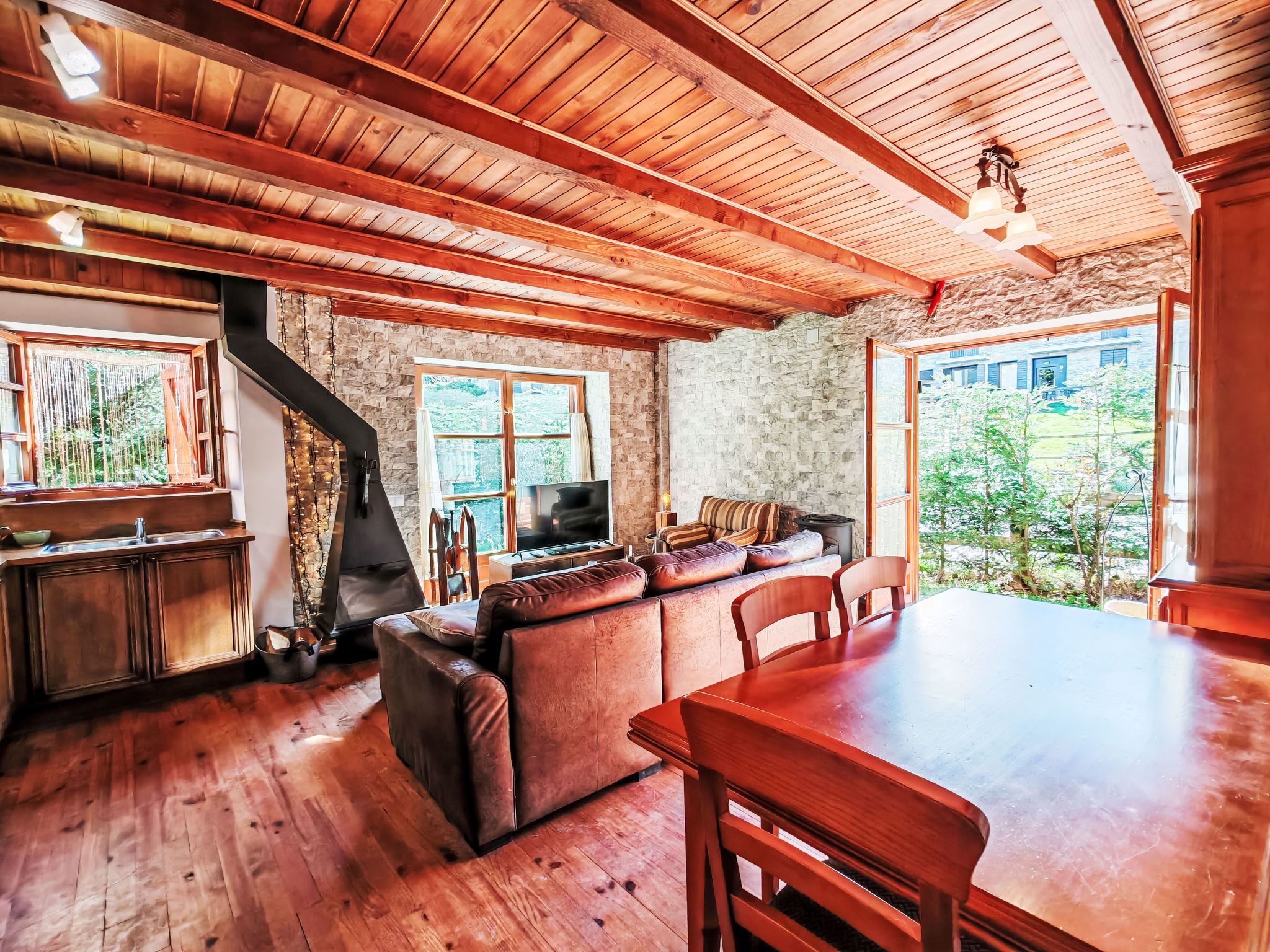 Un intérieur rustique avec un plafond en bois, des murs en pierre, une cheminée, un canapé, un téléviseur et une table à manger.