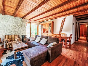 Ein gemütliches Wohnzimmer mit Steinwand, Holzbalken, einer Ledersofa, einem Esstisch und einem Kamin.