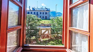 An open window with a view of a stone building, a wooden deck, and a mountain in the background. - Apartamento - Puig Falcó 3 by Interhome (Taüll)