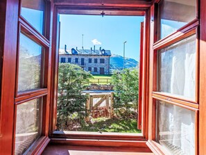 An open window with a view of a stone building, a wooden deck, and a mountain in the background. - Apartamento - Puig Falcó 3 by Interhome (Taüll)