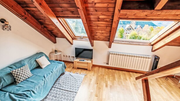 A loft-style room with a wooden ceiling, a sofa, a TV, a small table, and a radiator. - Dúplex Luminoso - Erta 12 by Interhome (Taüll)
