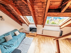 Ein Loft-Zimmer mit Holzbalkendecke, einer Couch, einem Fernseher, einem kleinen Tisch und einer Heizung.