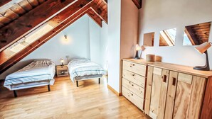 A loft bedroom with two beds, wooden ceiling beams, a wooden dresser, and a view through a skylight. - Dúplex Luminoso - Erta 12 by Interhome (Taüll)
