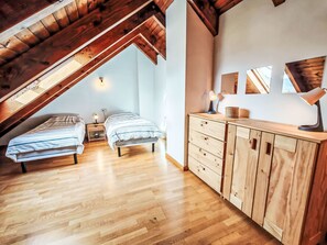 Ein Schlafzimmer im Loft-Stil mit zwei Betten, Holzbalken an der Decke, einer Holzkommode und Blick durch ein Dachfenster.