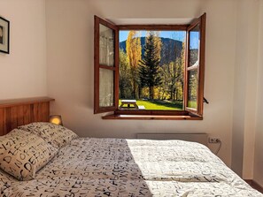 Ein Schlafzimmer mit großem Fenster, einem Bett mit gemusterten Betttextilien und einem Holzkopfende.