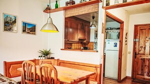 A wooden dining table with chairs, a hanging pendant light, wooden cabinets, and a kitchen area visible through an open door. - Escapad para parejas - Justal 2 by Interhome (Taüll)