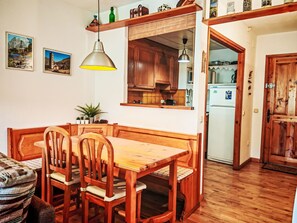 Ein Esszimmertisch mit Stühlen, eine hängende Pendelleuchte, Holzschränke und ein durch eine offene Tür sichtbarer Küchenbereich.