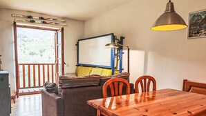 A cozy living area with a sofa, a wooden dining table, and chairs. There's a window with a view of greenery outside. - Escapad para parejas - Justal 2 by Interhome (Taüll)