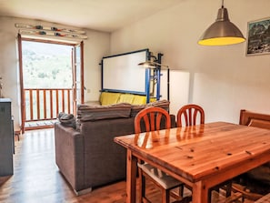 Ein gemütlicher Wohnbereich mit einer Couch, einem Holzesstisch und Stühlen. Ein Fenster bietet Blick auf die grüne Umgebung.