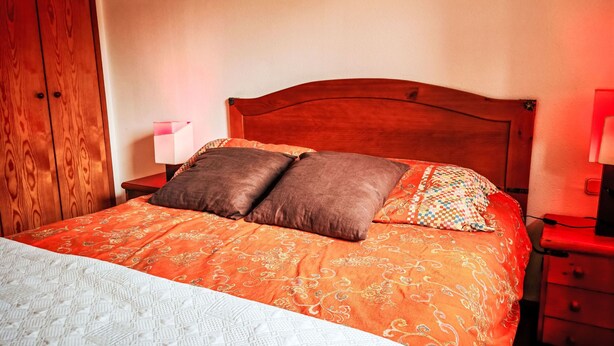 A bed with a patterned bedspread, two pillows, a nightstand with a lamp, and a wooden wardrobe. - Escapad para parejas - Justal 2 by Interhome (Taüll)