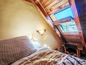 A bedroom with a sloped ceiling, a bed with a checkered pillow, a bedside lamp, and a view through a skylight. - Dúplex de Aigüestort -Falcó 6 by Interhome (Taüll)