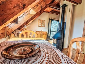 A cozy attic room with a wooden ceiling, a table with a tray, a chair, a small cabinet, and a black stove. - Dúplex de Aigüestort -Falcó 6 by Interhome (Taüll)
