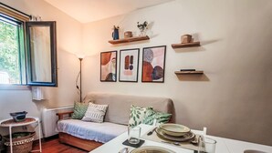 Een woonkamer met een bank, een eettafel gedekt met borden, kommen en bestek, en een raam met gordijnen.