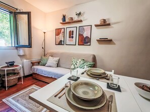 Ein Wohnzimmer mit einer Couch, einem Esstisch gedeckt mit Tellern, Schüsseln und Besteck, sowie einem Fenster mit Vorhängen.
